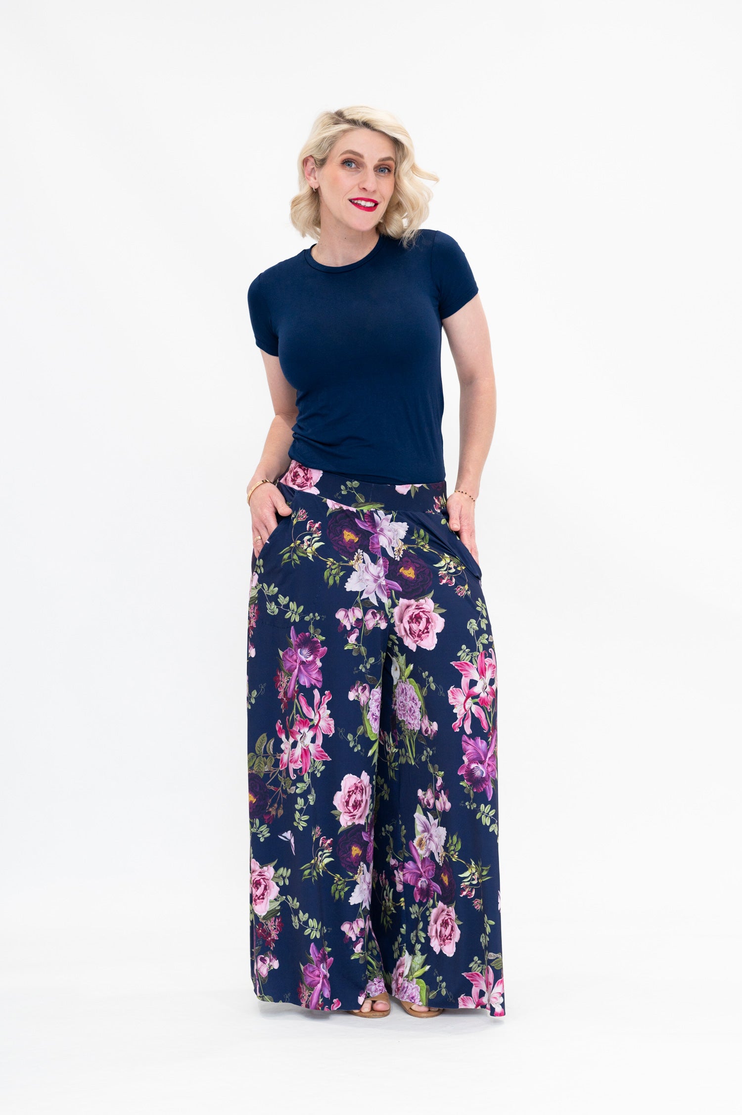 Model wearing Hazel palazzo pants by By Samantha Melbourne. Wide-leg, high-waisted style with pockets in a navy floral print with pink accents.