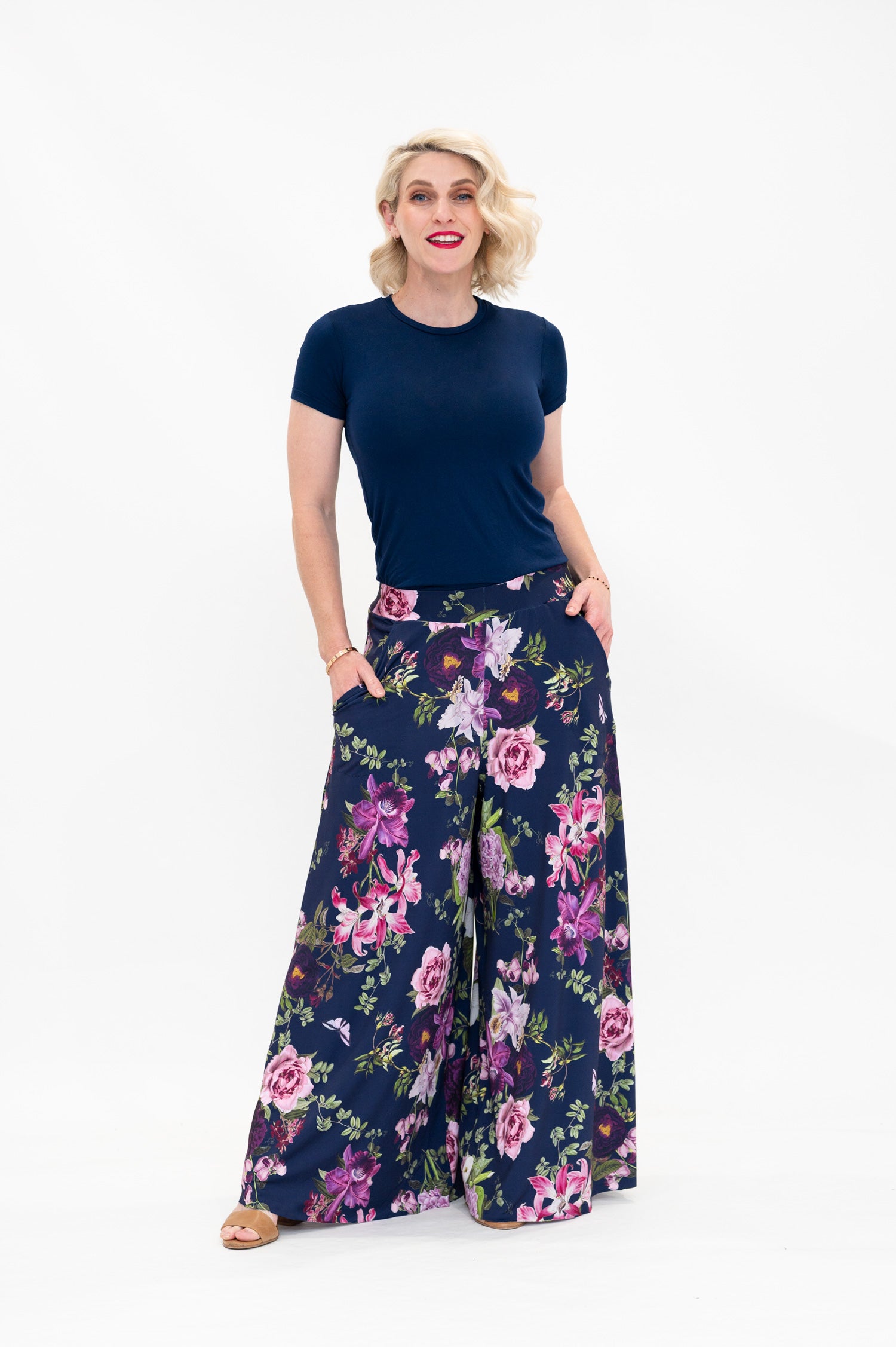 Model wearing Hazel palazzo pants by By Samantha Melbourne. Wide-leg, high-waisted style with pockets in a navy floral print with pink accents.