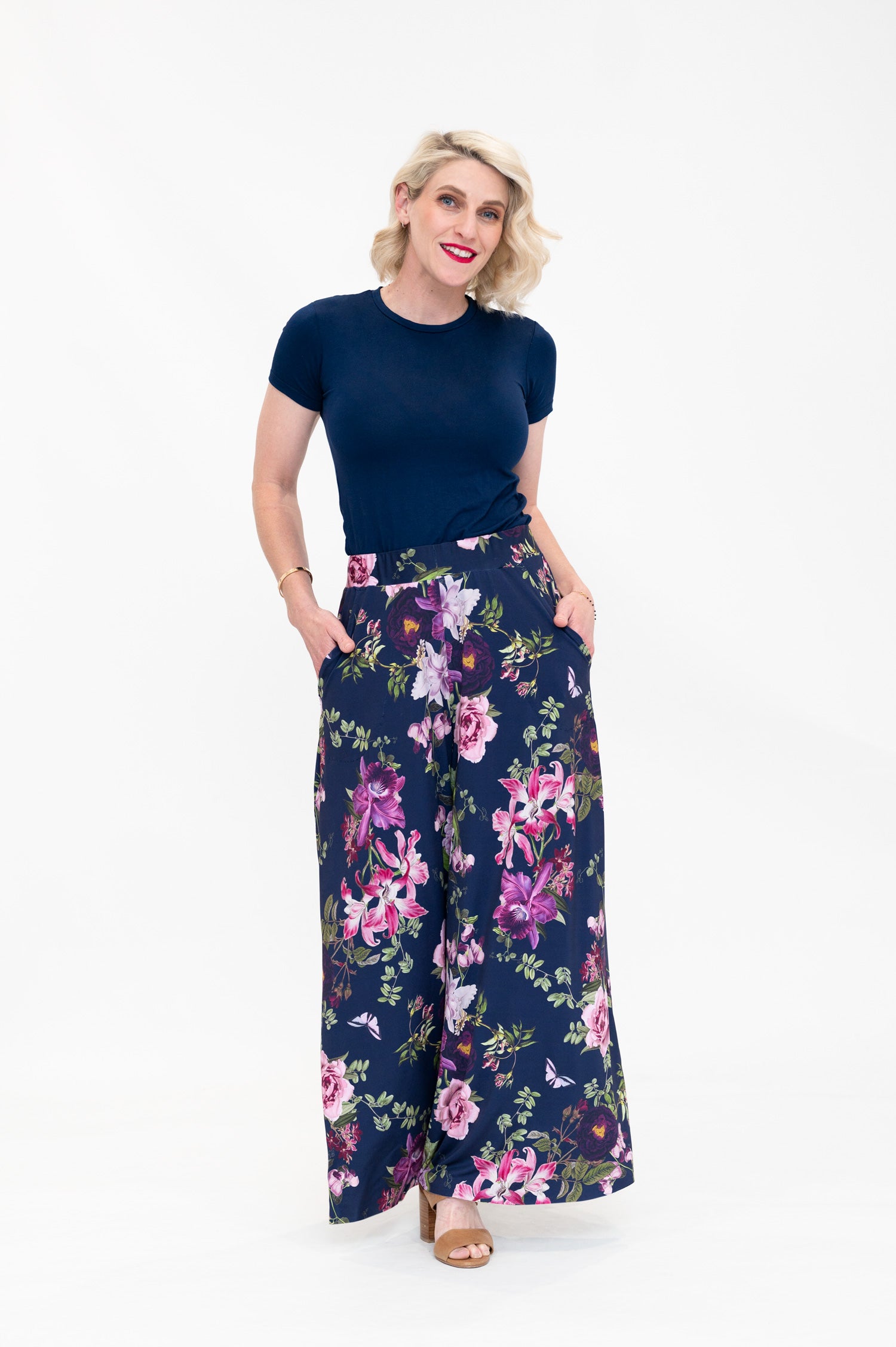 Model wearing Hazel palazzo pants by By Samantha Melbourne. Wide-leg, high-waisted style with pockets in a navy floral print with pink accents.