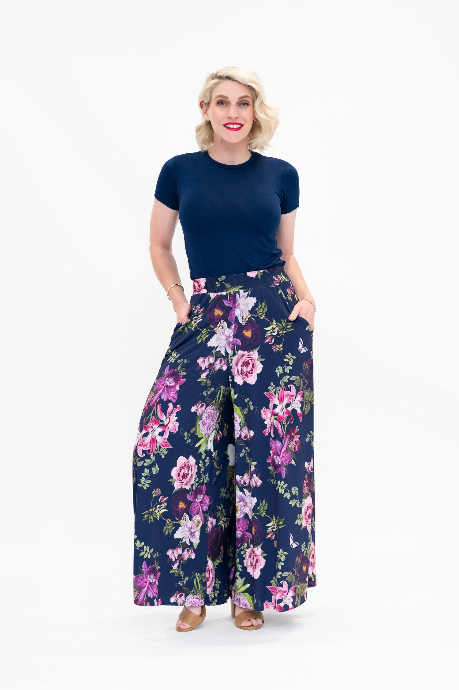 Model wearing Hazel palazzo pants by By Samantha Melbourne. Wide-leg, high-waisted style with pockets in a navy floral print with pink accents.
