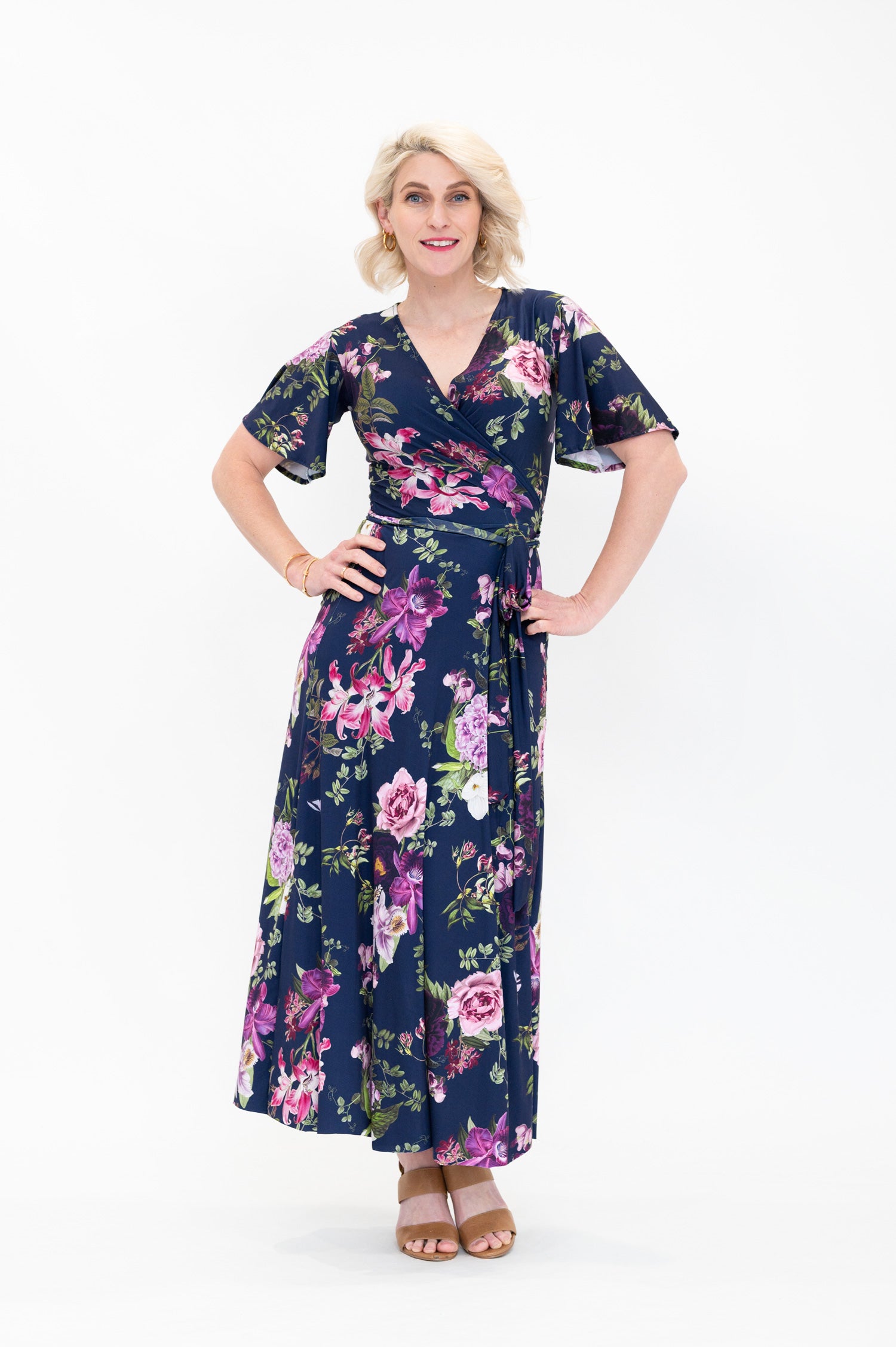 Model wearing the Hazel midi floral wrap dress with flutter sleeves by By Samantha Melbourne. Curve-friendly fit with a deep navy base and pink botanical print.