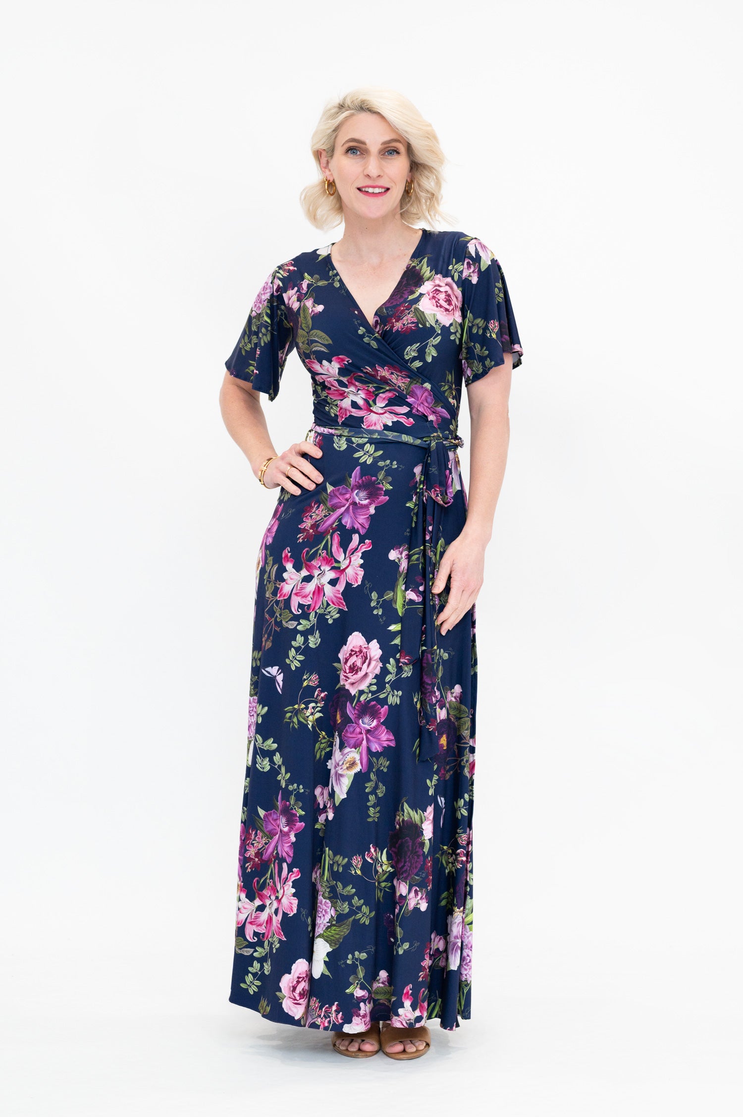Model wearing the Hazel maxi floral wrap dress with 3/4 sleeves by By Samantha Melbourne. Curve-friendly fit with a deep navy base and pink botanical print.