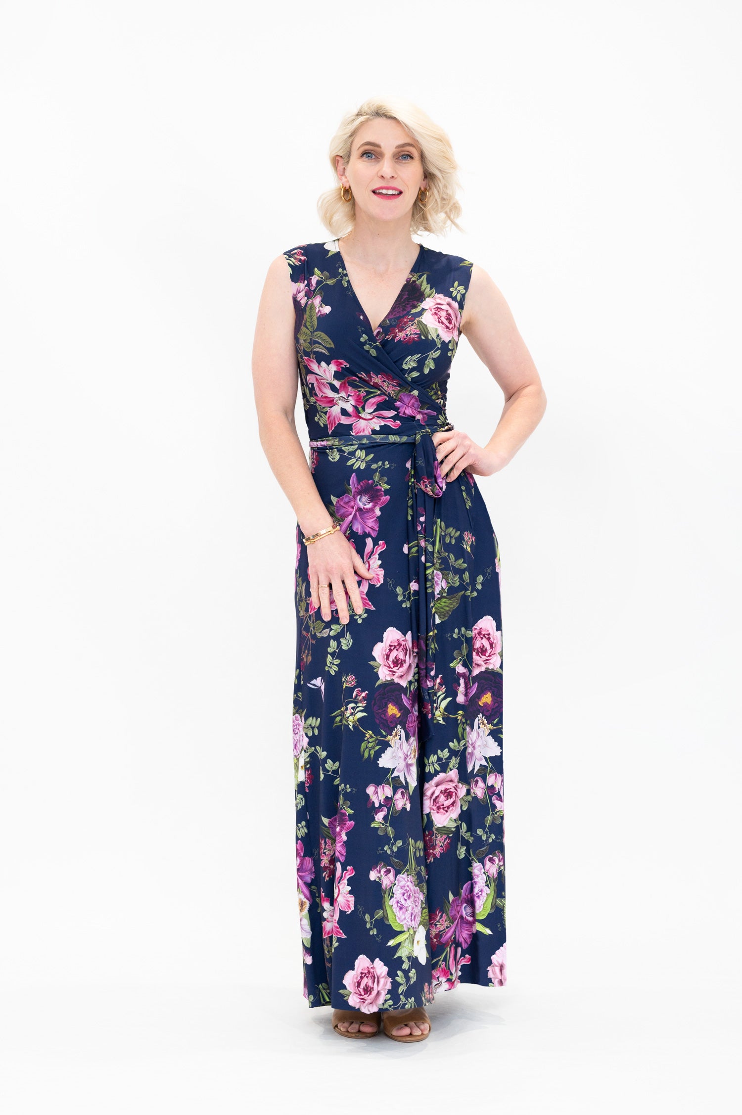 Model wearing the Hazel sleeveless maxi floral wrap dress by By Samantha Melbourne. Curve-friendly fit with a deep navy base and pink botanical print.
