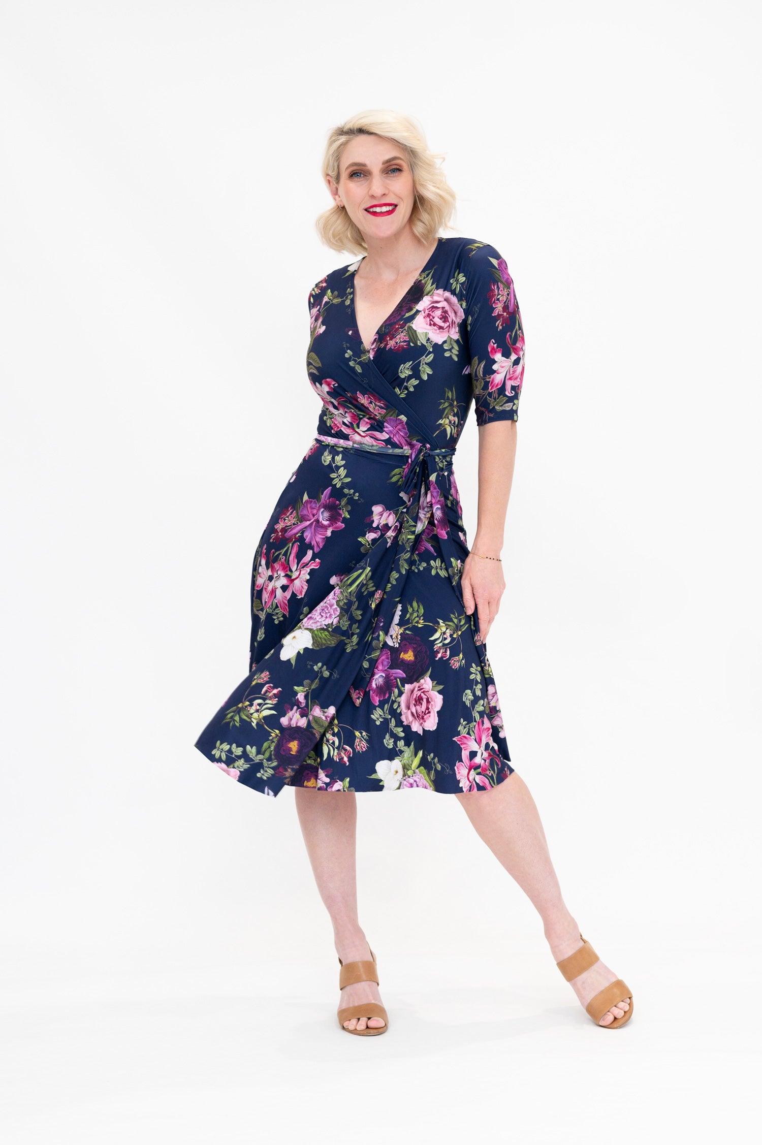 Model wearing the Hazel knee-length floral wrap dress with 3/4 sleeves by By Samantha Melbourne. Curve-friendly fit with a deep navy base and pink botanical print.