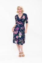 Model wearing the Hazel knee-length floral wrap dress with 3/4 sleeves by By Samantha Melbourne. Curve-friendly fit with a deep navy base and pink botanical print.