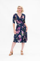 Model wearing the Hazel knee-length floral wrap dress with flutter sleeves by By Samantha Melbourne. Curve-friendly fit with a deep navy base and pink botanical print.