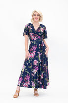 Model wearing the Hazel midi floral wrap dress with flutter sleeves by By Samantha Melbourne. Curve-friendly fit with a deep navy base and pink botanical print.