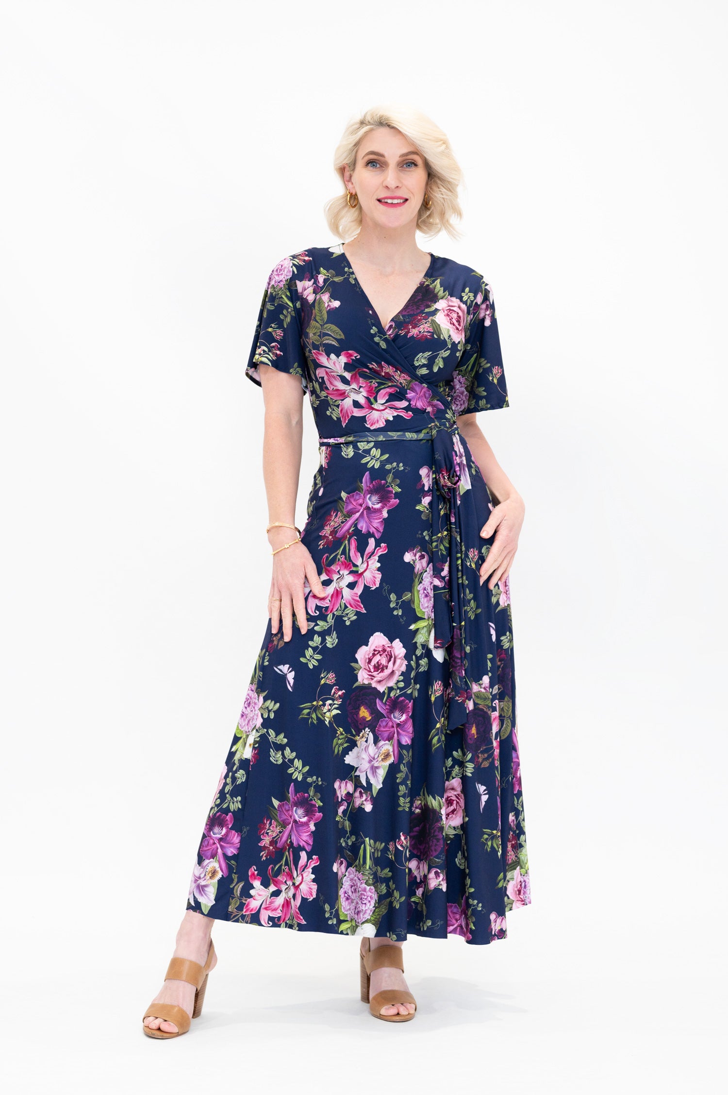 Model wearing the Hazel midi floral wrap dress with flutter sleeves by By Samantha Melbourne. Curve-friendly fit with a deep navy base and pink botanical print.