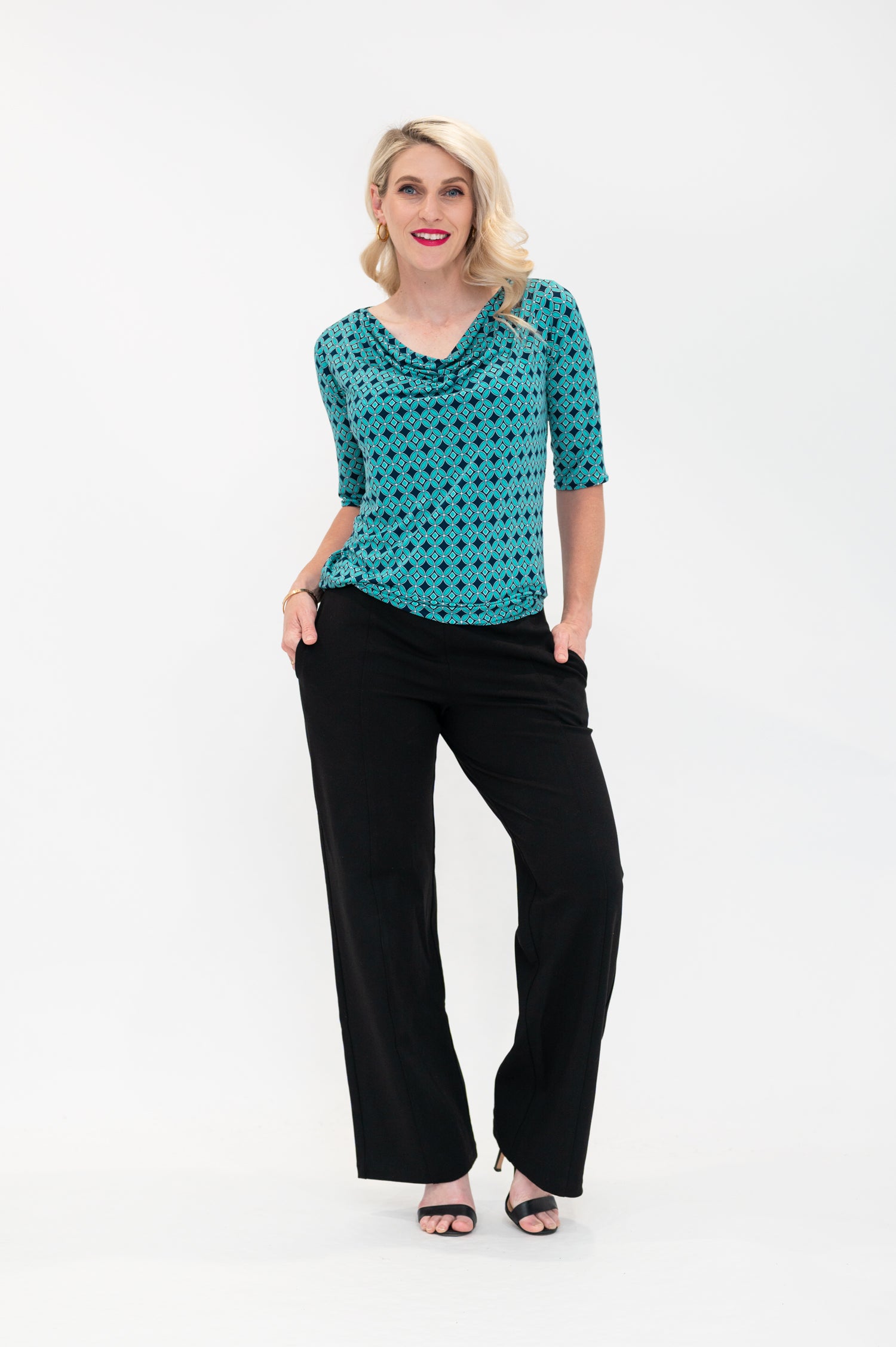 The female model wears a cowl neck top with 3/4 sleeves, the top is untucked in black pants. The print is small scale deep navy, white and teal geometric diamond shape pattern