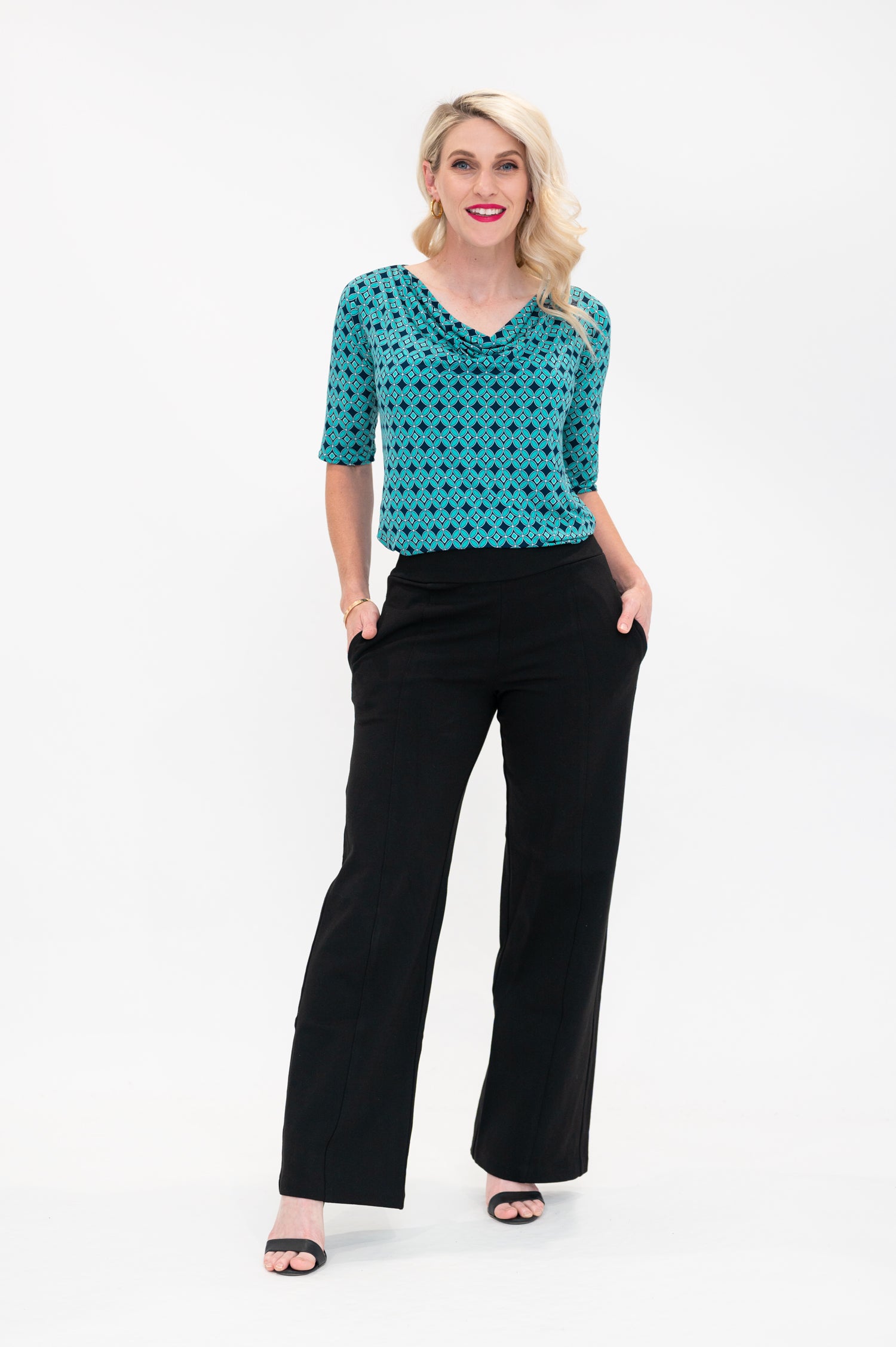 The female model wears a cowl neck top with 3/4 sleeves, the top is tucked into black pants. The print is small scale deep navy, white and teal geometric diamond shape pattern
