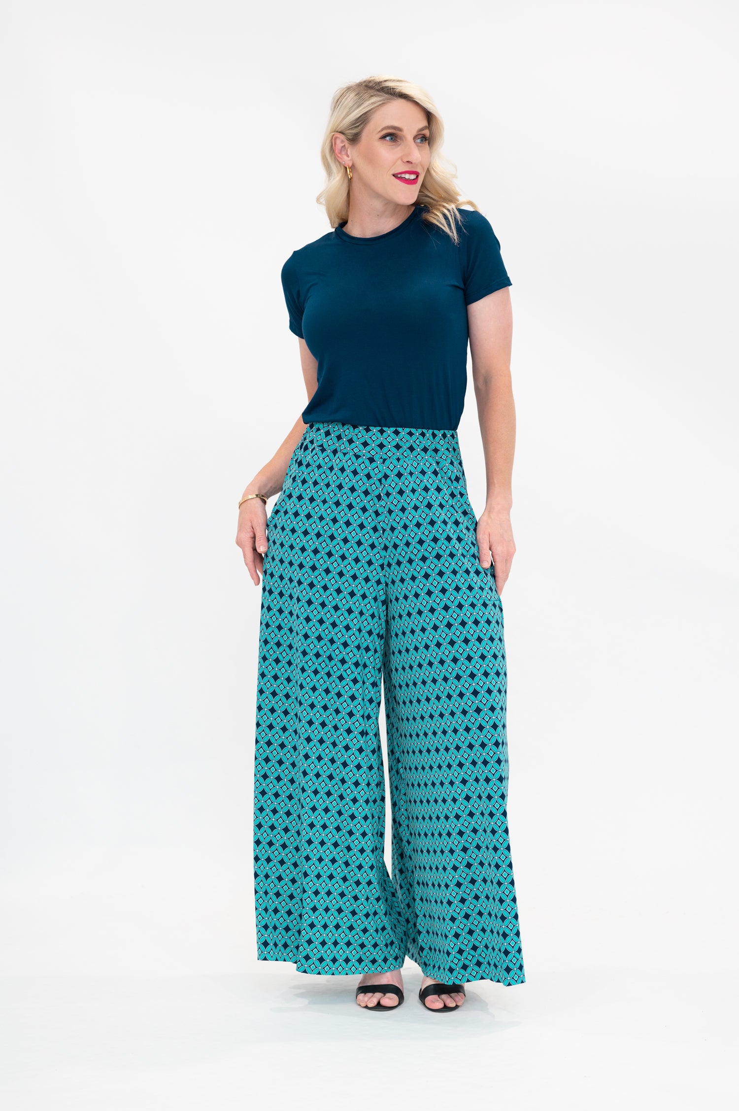 The female model wears a t-shirt in a Dark Teal colour tucked in palazzo pants. The print of the palazzo pants is a small-scale deep navy, white and teal geometric diamond shape pattern. Front view