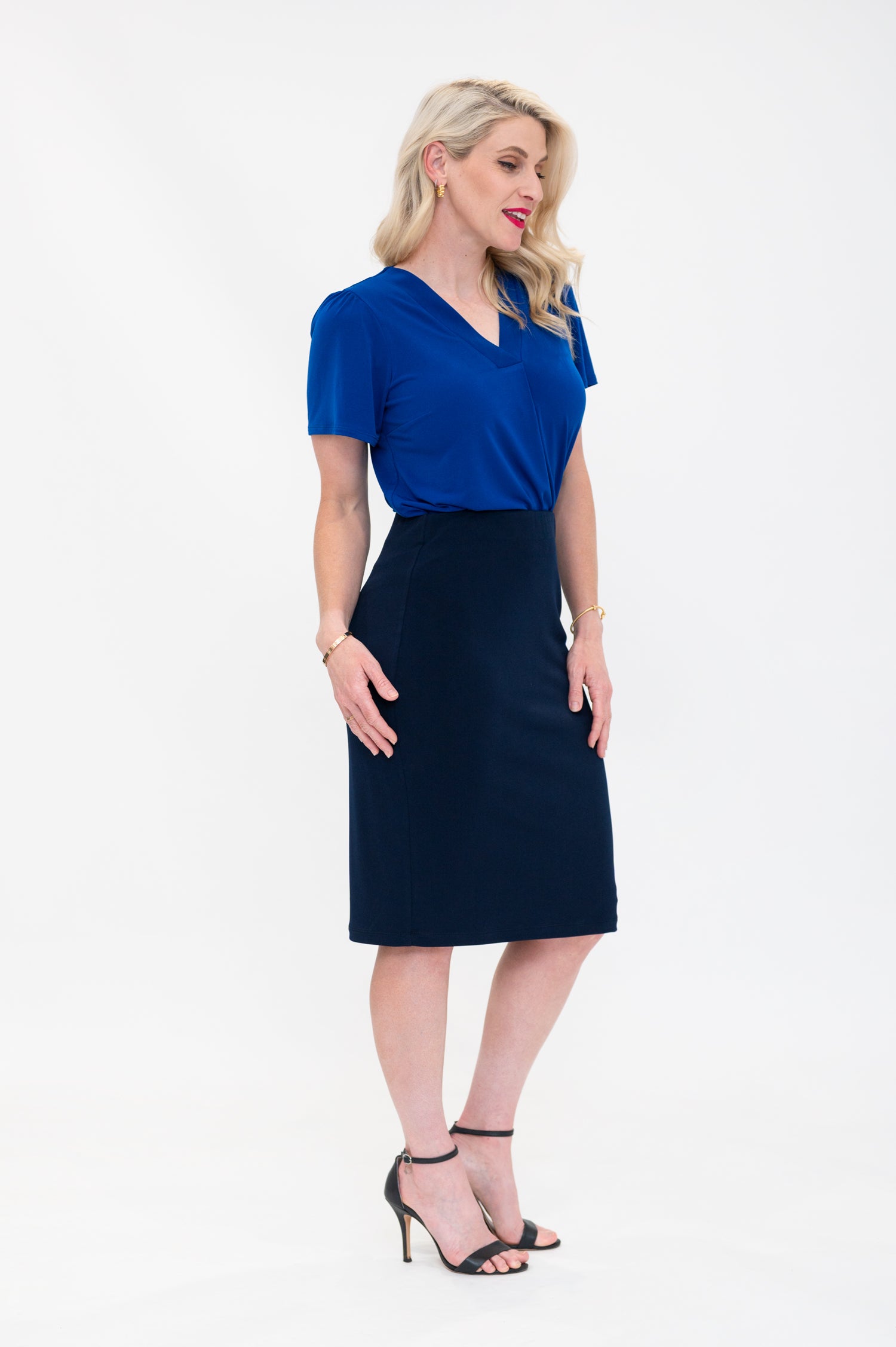 By Samantha Melbourne Officewear. Model wears Gina the V-neck blouse with flutter sleeve in cobalt blue with Andy pencil skirt in knee-length in navy. Side view