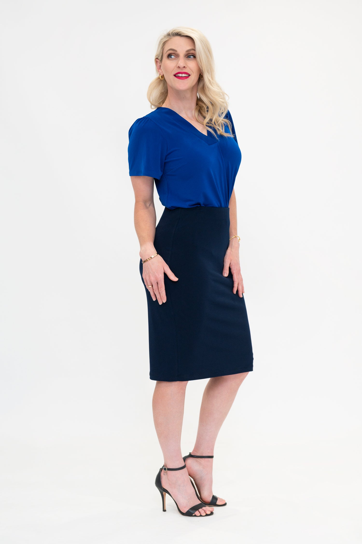 By Samantha Melbourne Officewear. Model wears Gina the V-neck blouse with flutter sleeve in cobalt blue with Andy pencil skirt in knee-length in navy. Side view
