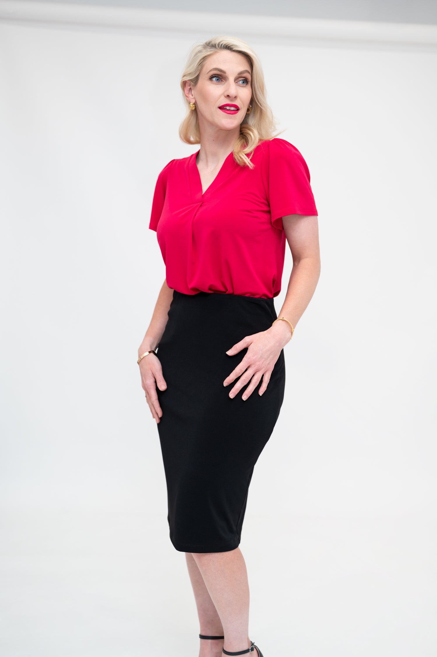 By Samantha Melbourne Officewear. Model wears Gina the V-neck blouse with flutter sleeve in granita raspberry red colour with Andy pencil skirt in knee-length in black. Side view