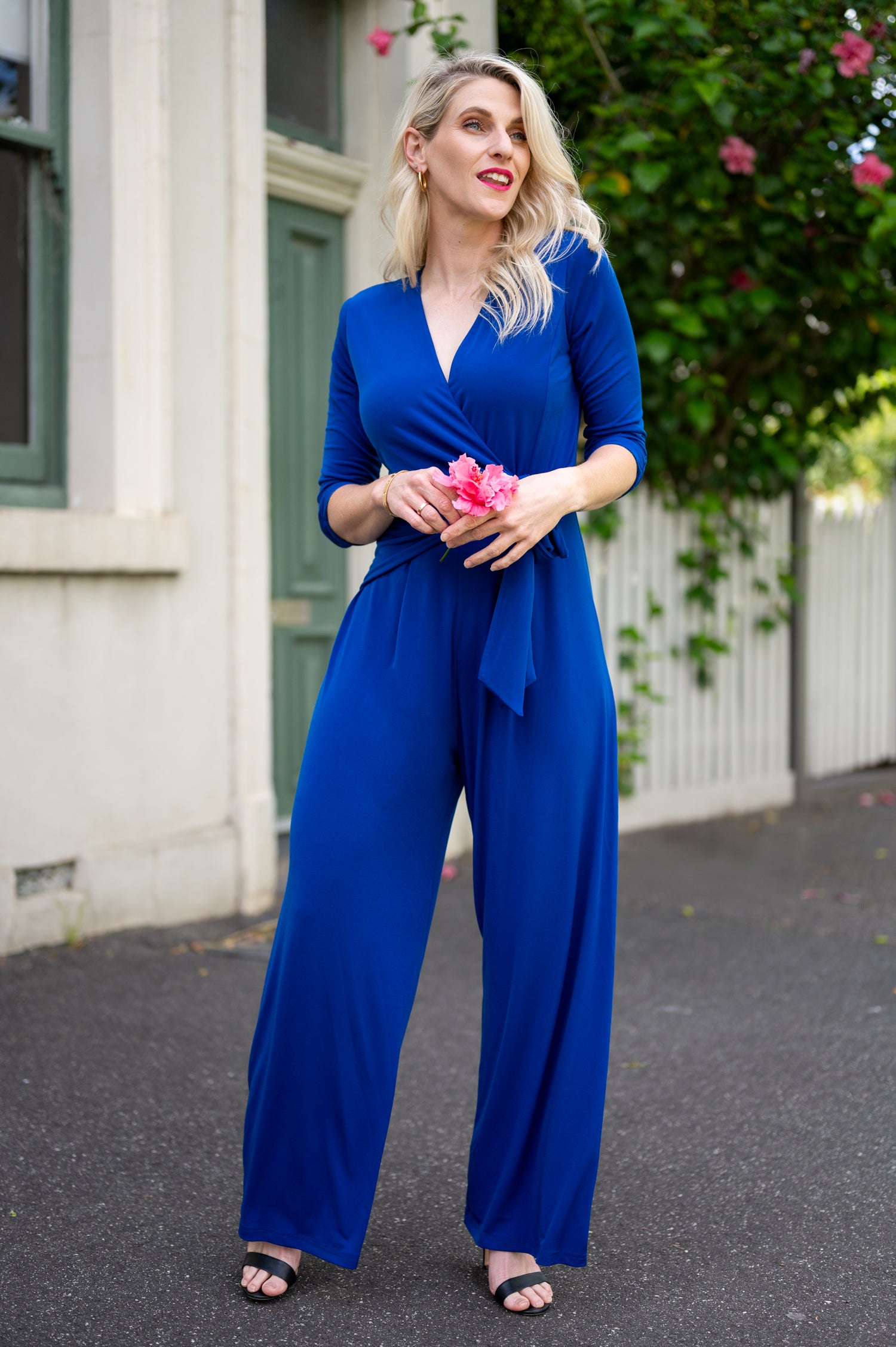 Female model in cobalt blue wrap jumpsuit outdoor. Front view