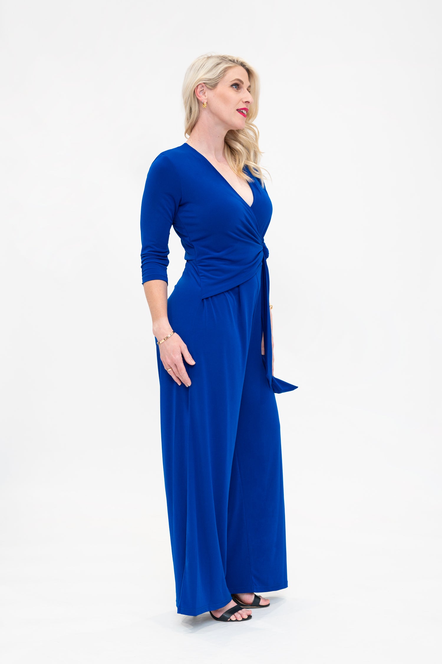 Female model in cobalt blue wrap jumpsuit. Side view