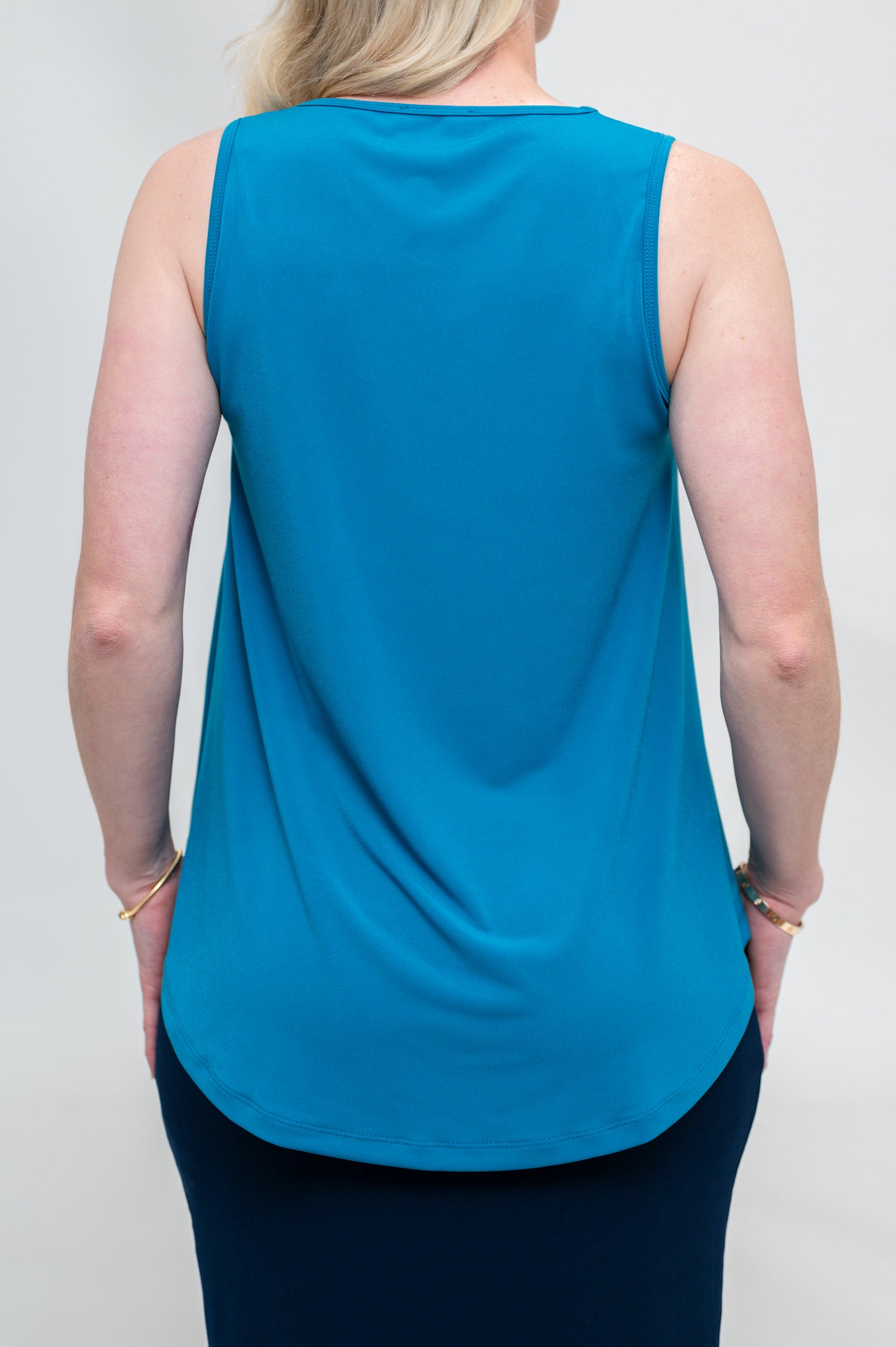 By Samantha Melbourne Erin Swing Singlet. Available in 3 colours. Made in Australia. Model wears Erin Singlet in Blue. Erin Singlet is sleeveless, features Round Crew Neck, Swing style and Relaxed fit, Hip length. Singlet is untucked and paired with By Samantha Melbourne Andy Pencil Skirt in Navy. Closeup of the back