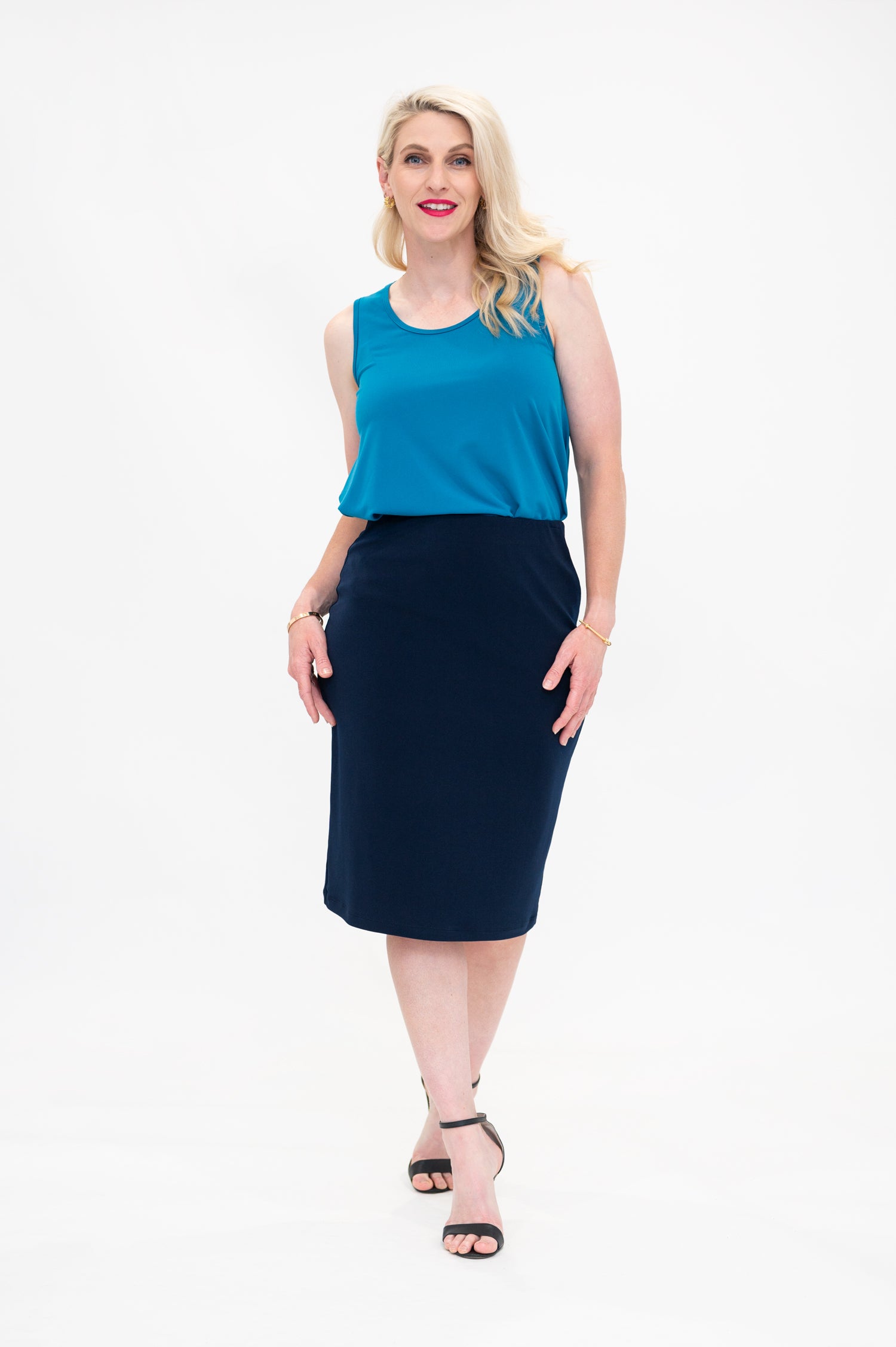 By Samantha Melbourne Erin Swing Singlet. Available in 3 colours. Made in Australia. Model wears Erin Singlet in Blue. Erin Singlet is sleeveless, features Round Crew Neck, Swing style and Relaxed fit, Hip length. Singlet is tucked and paired with By Samantha Melbourne Andy Pencil Skirt in Navy