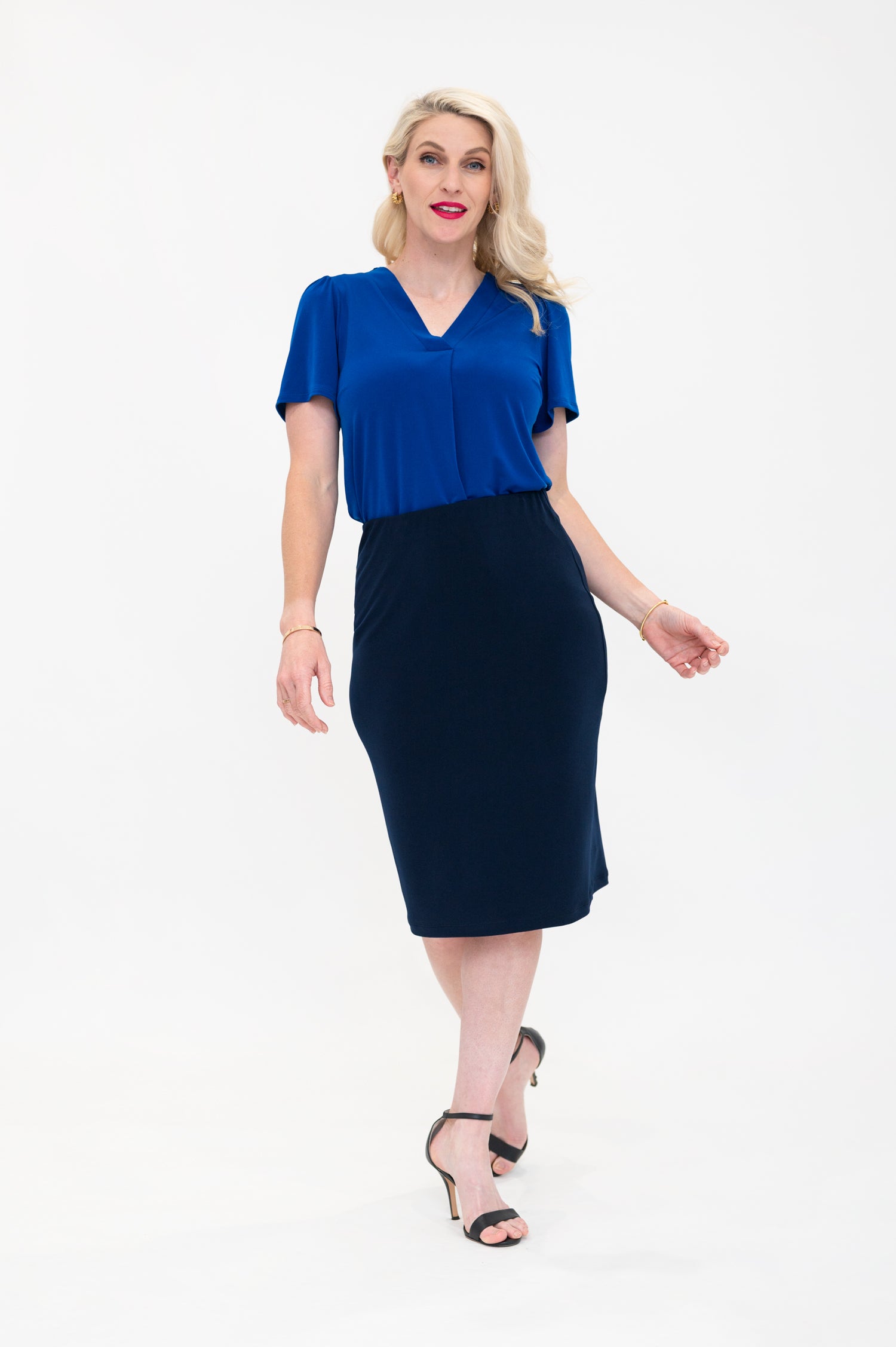 By Samantha Melbourne Officewear. Model wears Gina the V-neck blouse with flutter sleeve in cobalt blue with Andy pencil skirt in knee-length in navy. The blouse is tucked into skirt