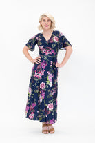 Model wearing the Hazel midi floral wrap dress with flutter sleeves by By Samantha Melbourne. Curve-friendly fit with a deep navy base and pink botanical print.