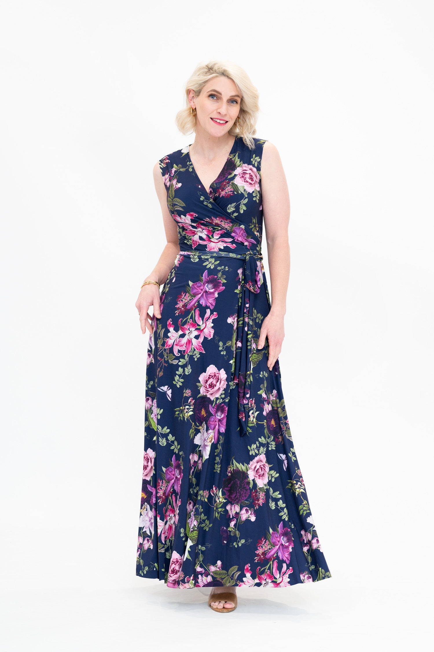 Model wearing the Hazel sleeveless maxi floral wrap dress by By Samantha Melbourne. Curve-friendly fit with a deep navy base and pink botanical print.