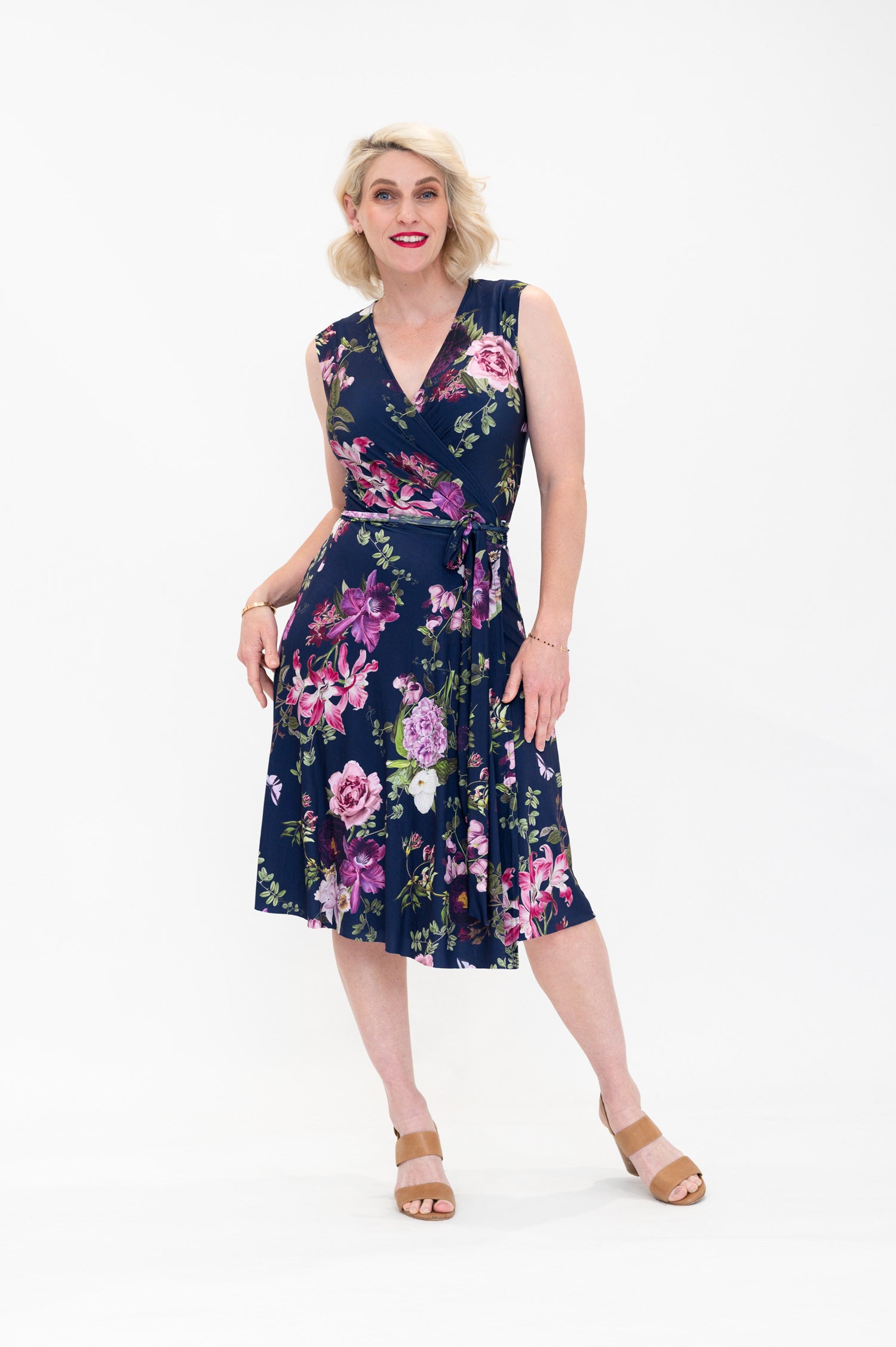 Model wearing the Hazel sleeveless knee-length floral wrap dress by By Samantha Melbourne. Curve-friendly fit with a deep navy base and pink botanical print.