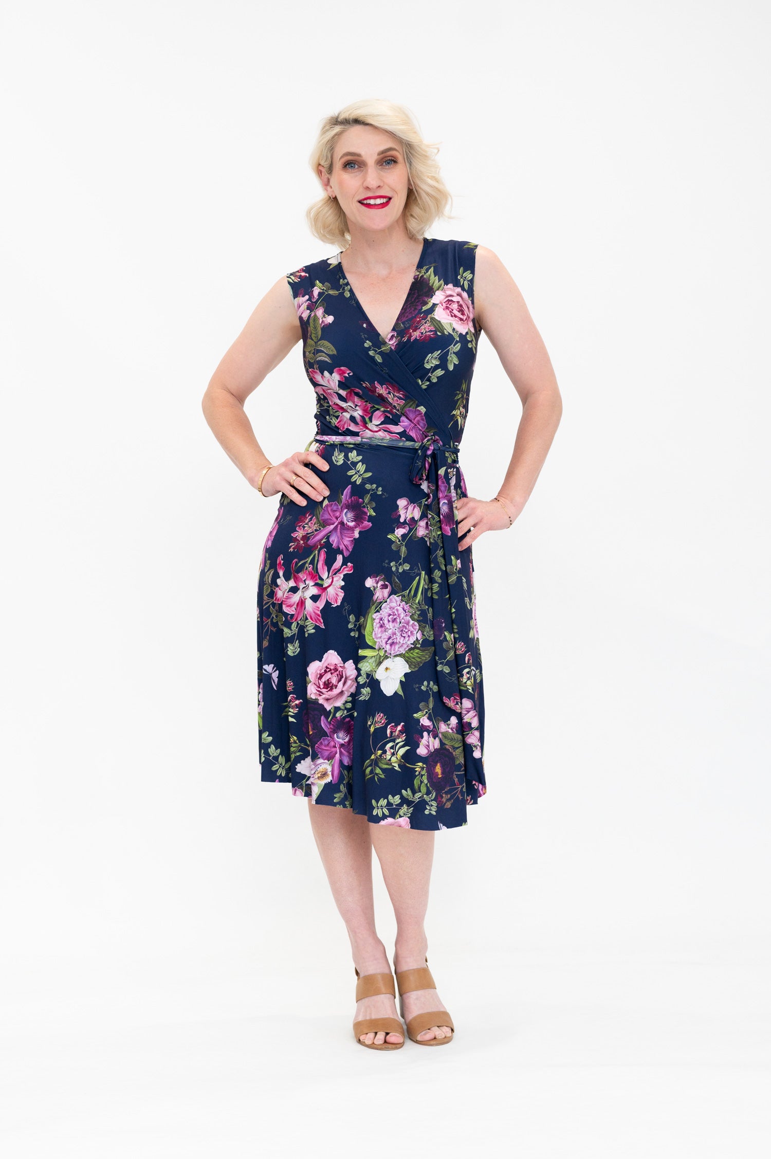 Model wearing the Hazel sleeveless knee-length floral wrap dress by By Samantha Melbourne. Curve-friendly fit with a deep navy base and pink botanical print.