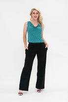 The female model wears a cowl neck top with no sleeves, the top is tucked into black pants. The print is small scale deep navy, white and teal geometric diamond shape pattern