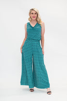 The female model wears a cowl neck top with no sleeves, the top is tucked in palazzo pants. The print is a small-scale deep navy, white and teal geometric diamond shape pattern. Front view