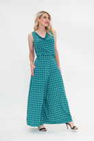 The female model wears a cowl neck top with no sleeves, the top is tucked in palazzo pants. The print is a small-scale deep navy, white and teal geometric diamond shape pattern. Side view