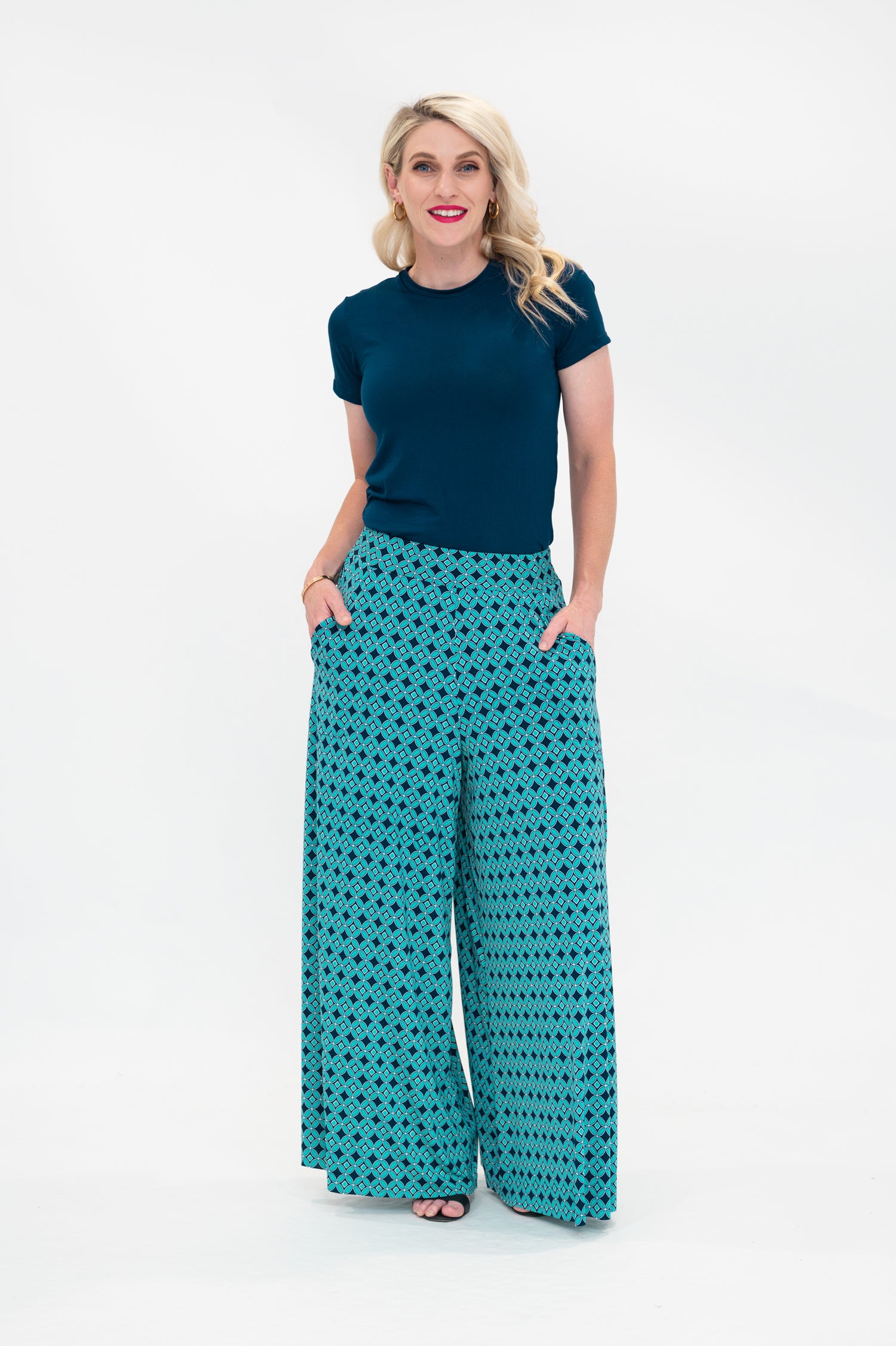 The female model wears a t-shirt in a Dark Teal colour tucked into palazzo pants. The print of the palazzo pants is a small-scale deep navy, white and teal geometric diamond shape pattern. Front view