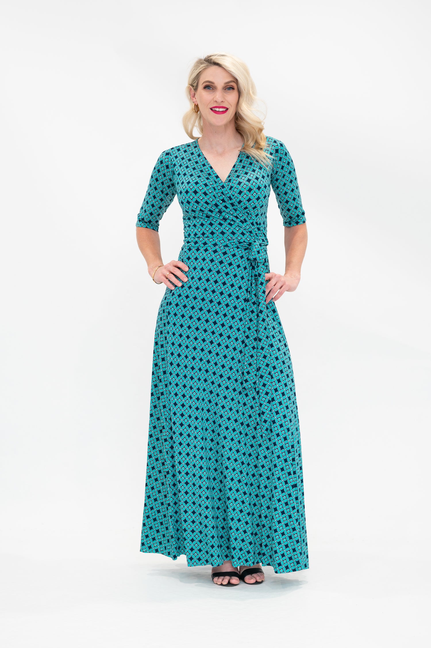 The female model wears a wrap dress in maxi length (floor length) with 3/4 sleeves. The print is a small-scale deep navy, white and teal geometric diamond shape pattern. Front view