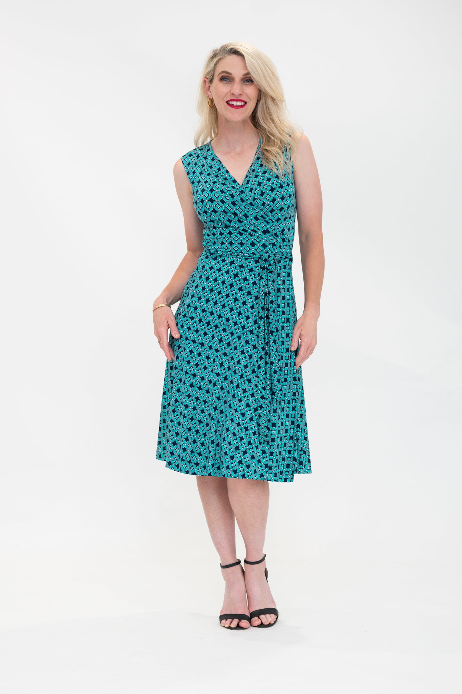 The female model wears a wrap dress in knee length with no sleeves. The print is a small-scale deep navy, white and teal geometric diamond shape pattern. Front view