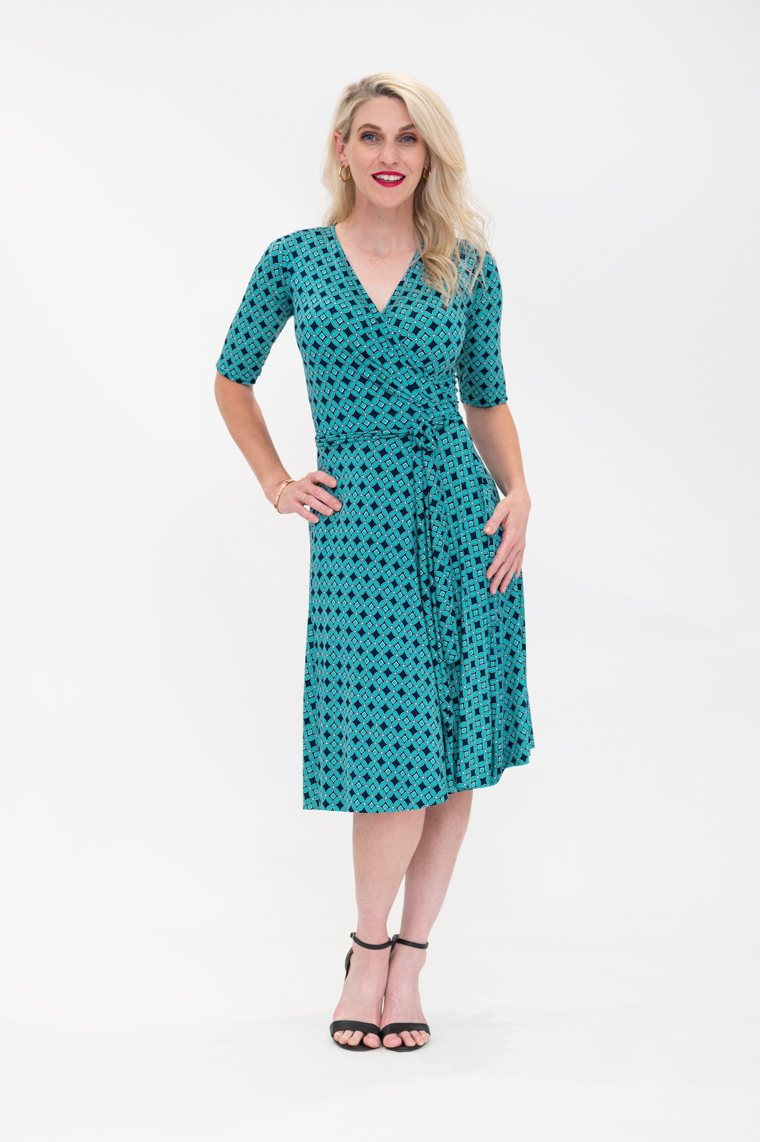  The female model wears a wrap dress in knee length with 3/4 sleeves. The print is a small-scale deep navy, white and teal geometric diamond shape pattern. Front view