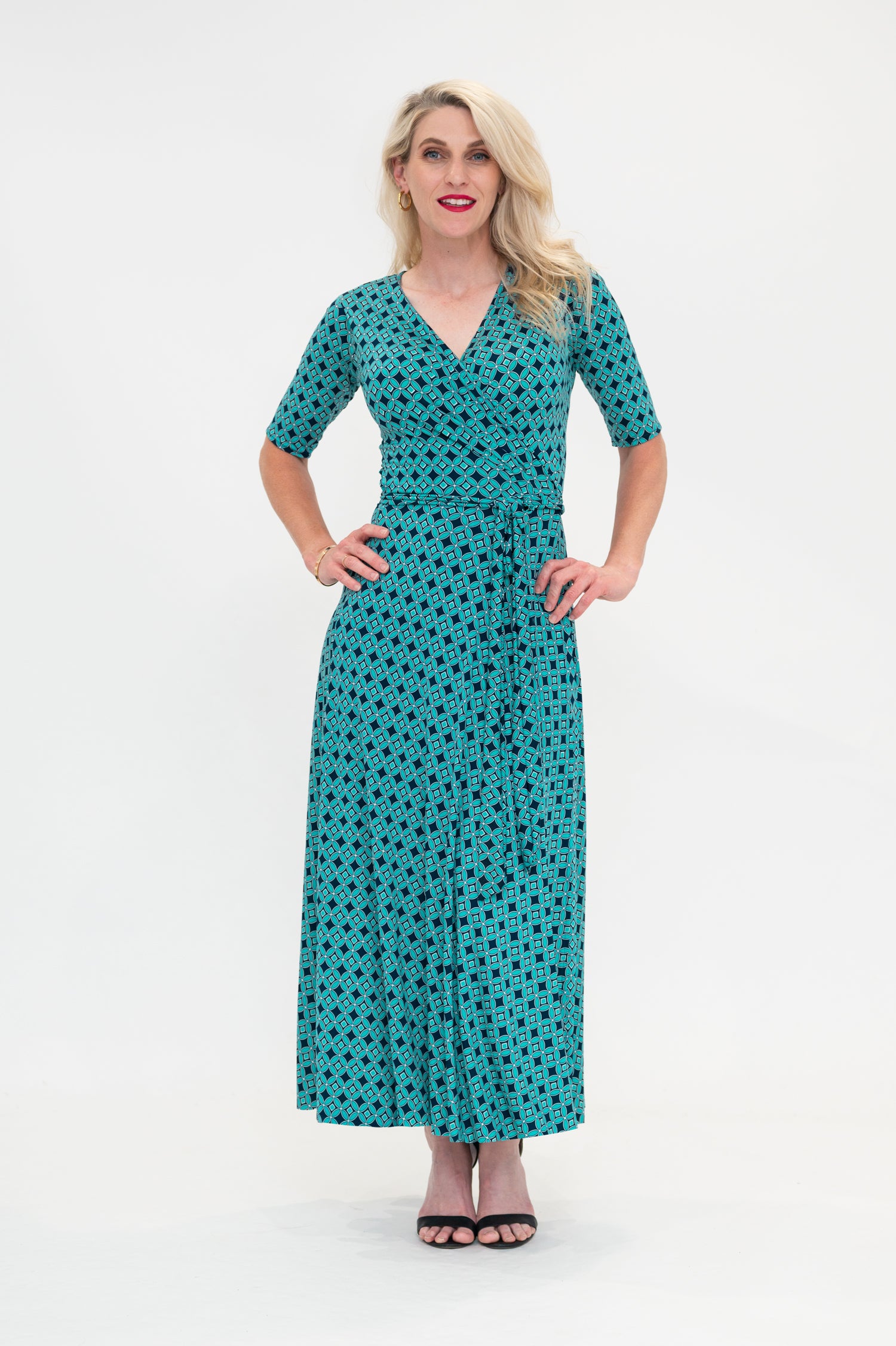 The female model wears a wrap dress in midi length (ankle length) with 3/4 sleeves. The print is a small-scale deep navy, white and teal geometric diamond shape pattern. Front view