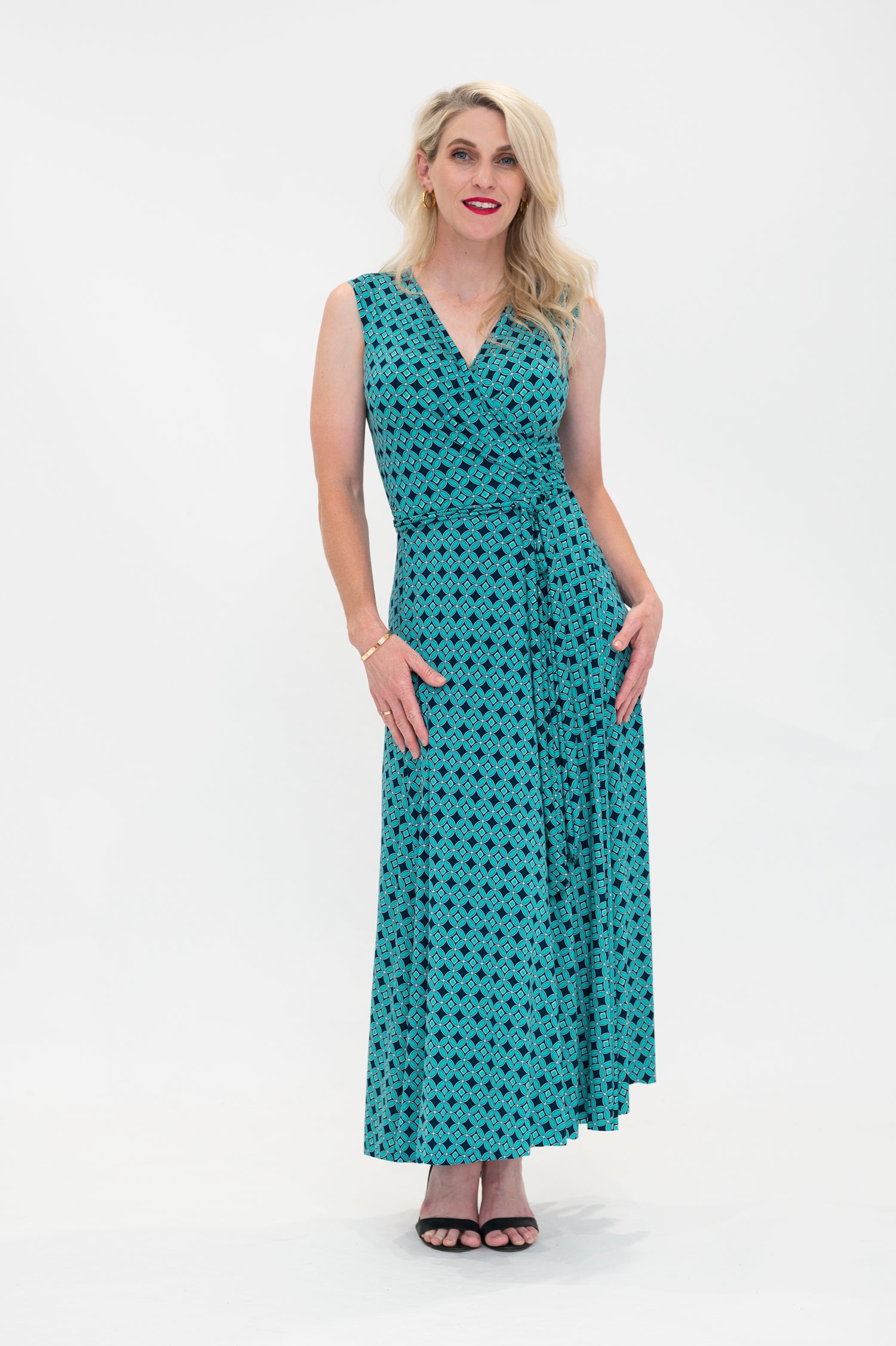 The female model wears a wrap dress in midi length (ankle length) with no sleeves. The print is a small-scale deep navy, white and teal geometric diamond shape pattern. Front view