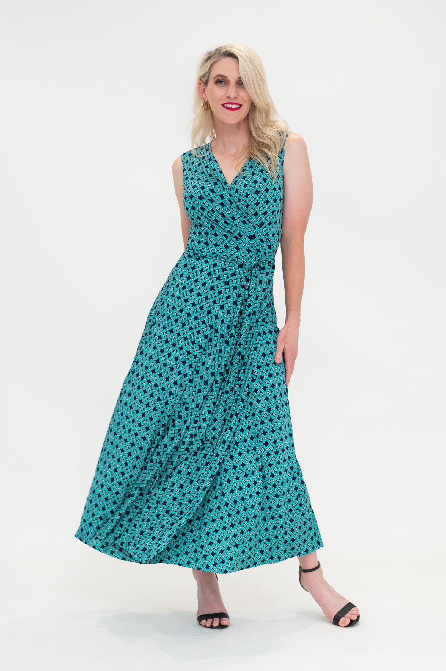 The female model wears a wrap dress in midi length (ankle length) with no sleeves. The print is a small-scale deep navy, white and teal geometric diamond shape pattern. Front view